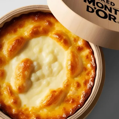 Mont d’Or au four très coulant dans sa boîte, avec une surface dorée et crémeuse, entouré de pain et pommes de terre.