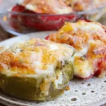 Poivrons rouges et jaunes farcis au fromage gratiné, cuits au four et servis dans un plat de cuisson.